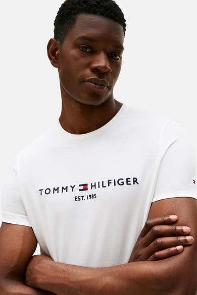 White short-sleeve T-shirt by TOMMY JEANS with navy logo and red flag, worn by model in front view