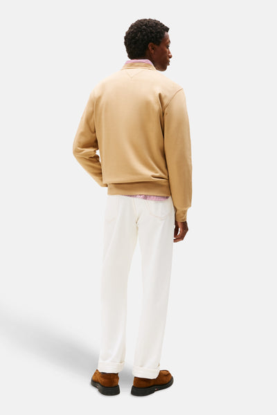 Beige sweatshirt van TOMMY HILFIGER met ronde hals, gedragen over een gestreept overhemd en een witte spijkerbroek.