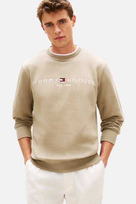 Kaki sweatshirt van TOMMY HILFIGER, met geborduurd logo op de voorkant, gedragen met een witte broek en zwarte loafers.