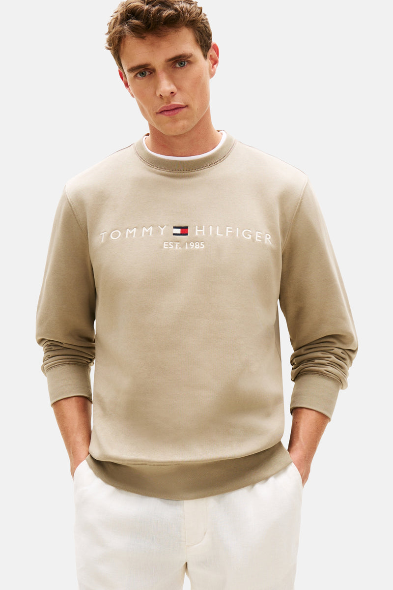 Kaki sweatshirt van TOMMY HILFIGER, met geborduurd logo op de voorkant, gedragen met een witte broek en zwarte loafers.
