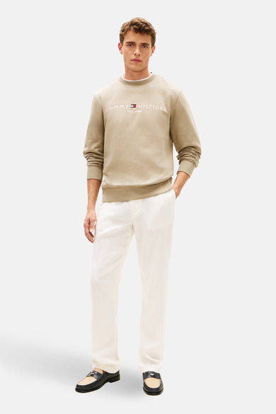Sweat-shirt kaki de TOMMY HILFIGER, avec logo brodé sur le devant, porté avec un pantalon blanc et des mocassins noirs.