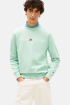 Sweat-shirt vert à col rond de TOMMY HILFIGER, avec logo brodé, porté sur une chemise en denim et un pantalon blanc.
