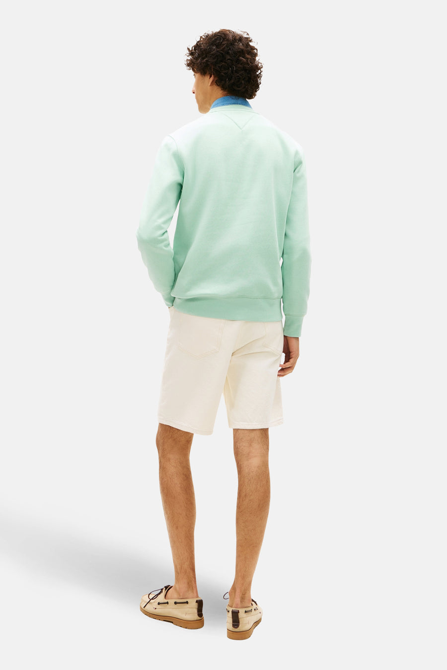 Sweat vert par TOMMY HILFIGER, avec col rond et manches longues, porté avec un short beige et des chaussures bateau.