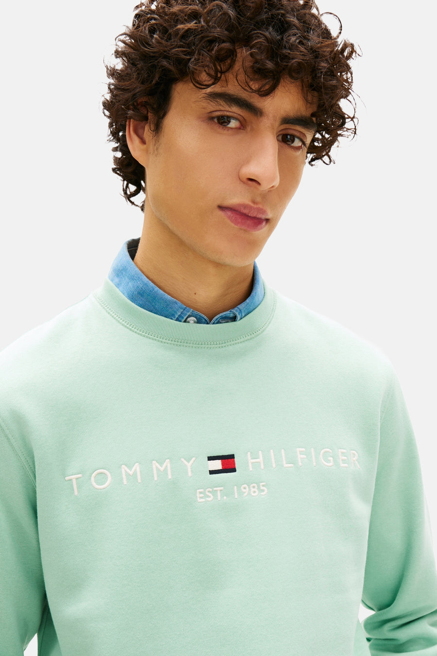 Sweat vert de TOMMY HILFIGER, avec inscription de la marque et porté sur une chemise en jean