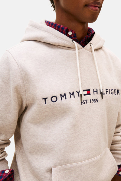 Beige hoodie van Tommy Hilfiger, witte trekkoord en geborduurd logo op de voorkant, gedragen met een geruit overhemd.