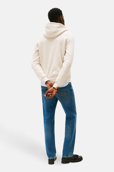Sweat écru de TOMMY HILFIGER avec capuche, porté avec une chemise rayée, un jean bleu et des mocassins noirs.