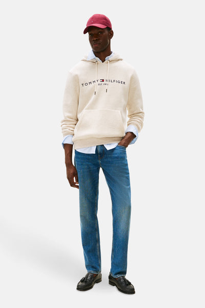 Sweat-shirt écru à capuche de Tommy Hilfiger, porté avec une chemise rayée bleu et un jean décontracté.