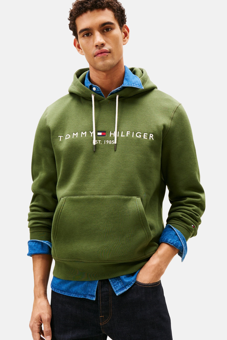 Sweat-shirt vert par TOMMY HILFIGER avec capuche et logo de la marque sur le devant, porté avec une chemise en jean.