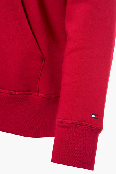 Red crewneck sweatshirt by Tommy Hilfiger, featuring ribbed cuffs and a small flag logo on the sleeve, close-up side view.