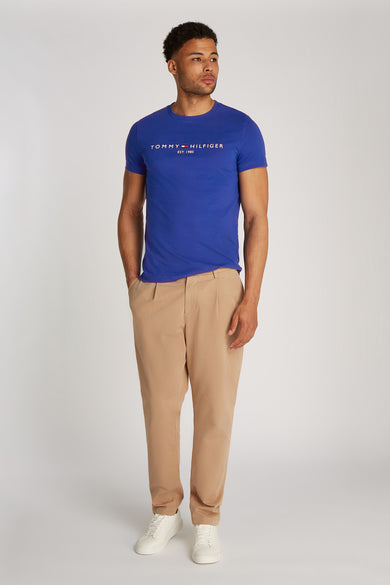 Blauw T-shirt met korte mouwen van TOMMY HILFIGER, met logo op de voorkant, gedragen met een beige broek en witte sneakers.