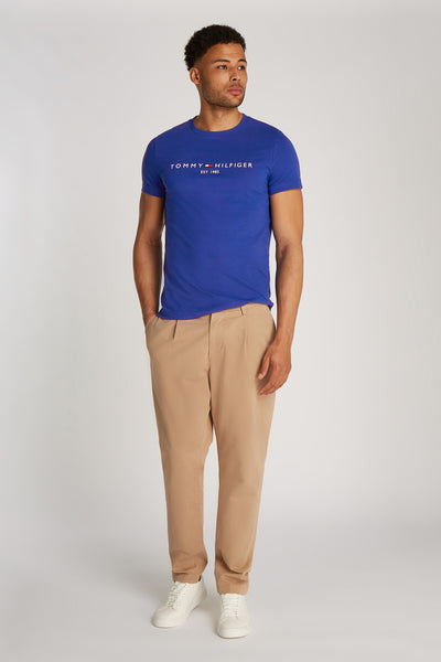 Blauw T-shirt met korte mouwen van TOMMY HILFIGER, met logo op de voorkant, gedragen met een beige broek en witte sneakers.