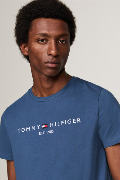 Blauw T-shirt met korte mouwen van TOMMY HILFIGER met wit logo op de voorkant, gedragen door een man.