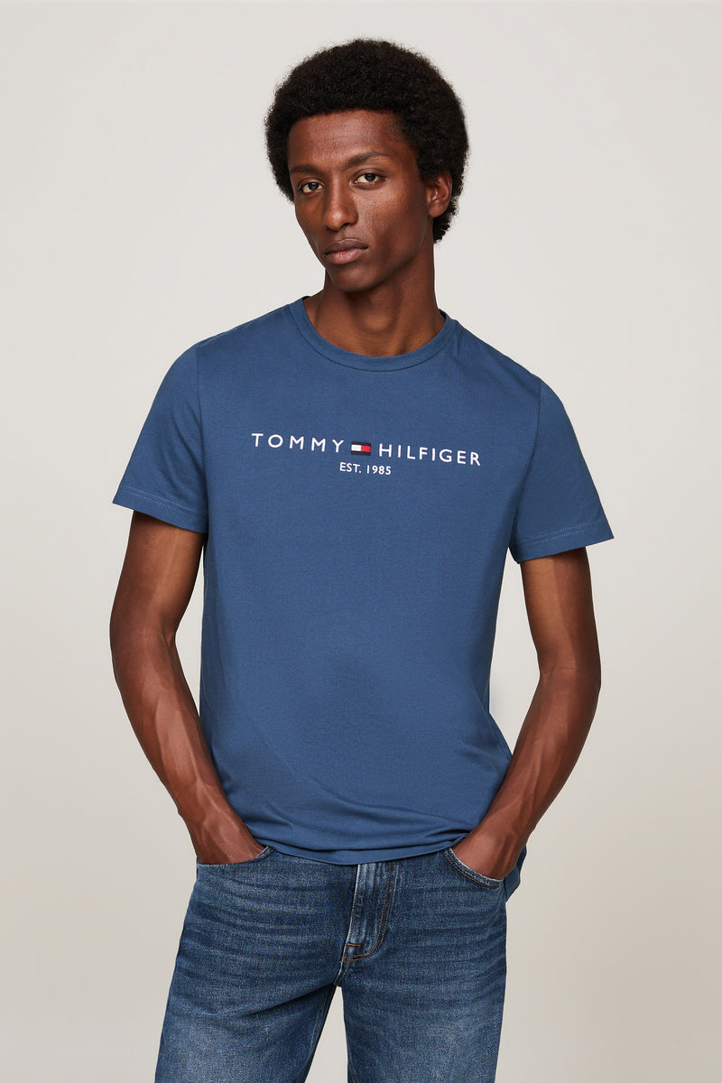 T-shirt bleu à manches courtes de TOMMY HILFIGER, porté avec un jean bleu, les mains dans les poches.
