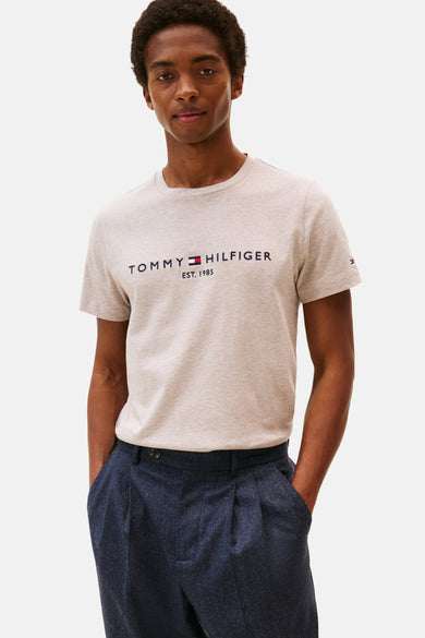 Beige T-shirt met korte mouwen van Tommy Hilfiger met geborduurd logo op de voorkant, gedragen met een marineblauwe broek.