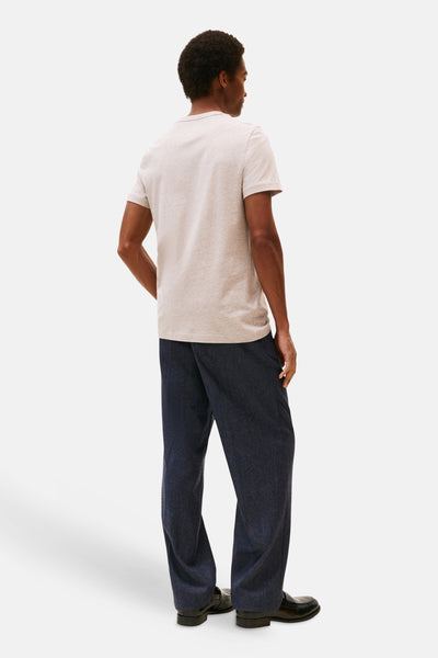 Beige T-shirt met korte mouwen van TOMMY HILFIGER, gedragen met een wijde donkerblauwe broek en zwarte schoenen.