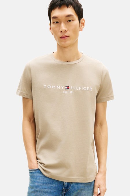 Beige T-shirt met korte mouwen van TOMMY HILFIGER, gedragen met een blauwe jeans en bootschoenen.