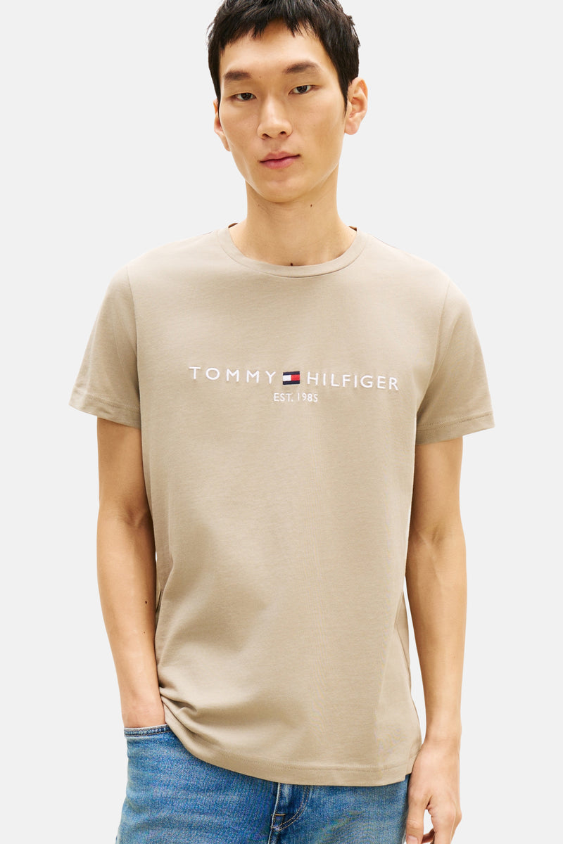 T-shirt beige à manches courtes de TOMMY HILFIGER, avec logo sur le devant et porté avec un jean.