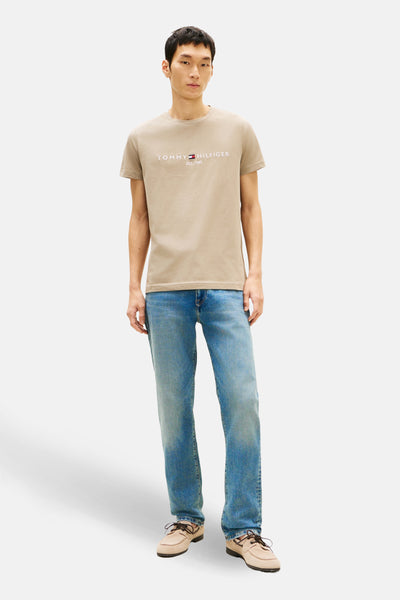 T-shirt à manches courtes beige de TOMMY HILFIGER, porté avec un jean bleu et des chaussures bateau.