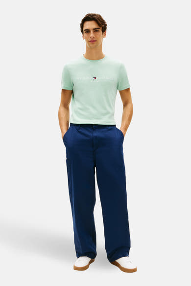 T-shirt à manches courtes vert de TOMMY HILFIGER, porté avec un pantalon bleu ample et des baskets blanches.