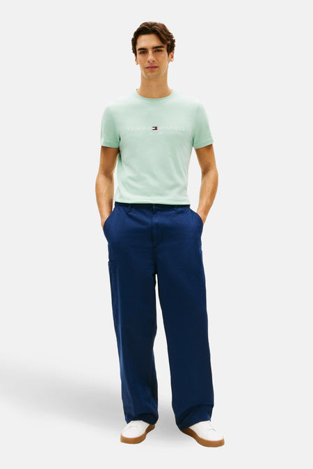 T-shirt à manches courtes vert de TOMMY HILFIGER, porté avec un pantalon bleu ample et des baskets blanches.