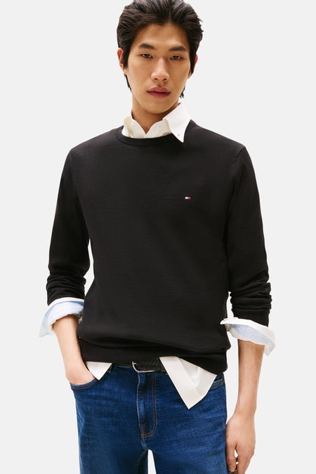 Zwarte rondehals trui van Tommy Hilfiger, gedragen over een wit overhemd en een blauwe spijkerbroek.