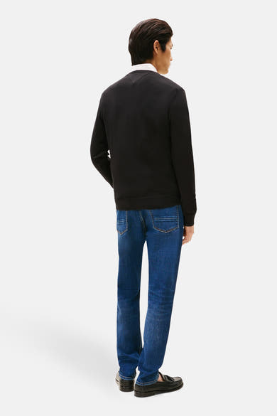 Zwarte rondehals trui van Tommy Hilfiger, gedragen met een wit overhemd en donkerblauwe jeans.