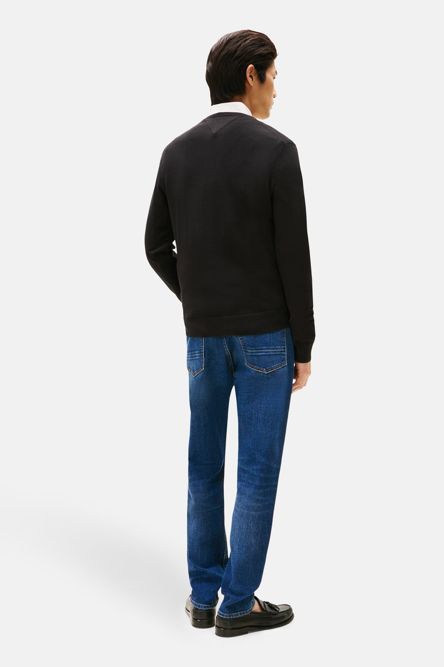 Zwarte rondehals trui van Tommy Hilfiger, gedragen met een wit overhemd en donkerblauwe jeans.