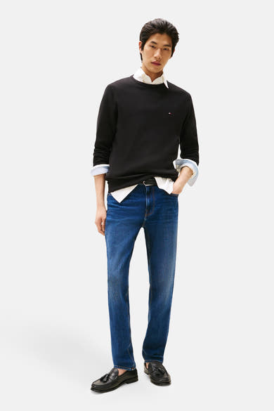 Zwarte rondehals trui van Tommy Hilfiger, gedragen met een witte blouse met opgerolde mouwen en een blauwe jeans.