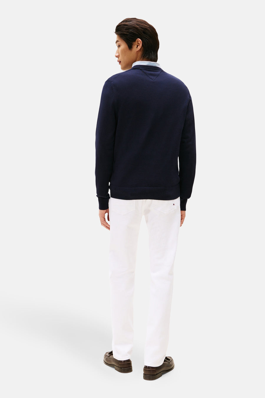 Pull à col rond bleu de Tommy Hilfiger, porté avec un pantalon blanc et des mocassins marron.