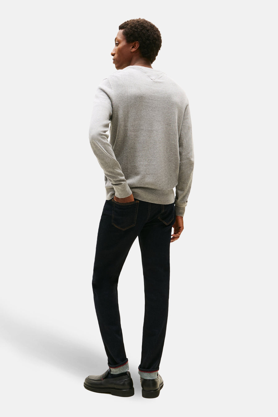 Grijze rondehals trui van Tommy Hilfiger, gedragen met een donkerblauwe jeans en zwarte loafers.