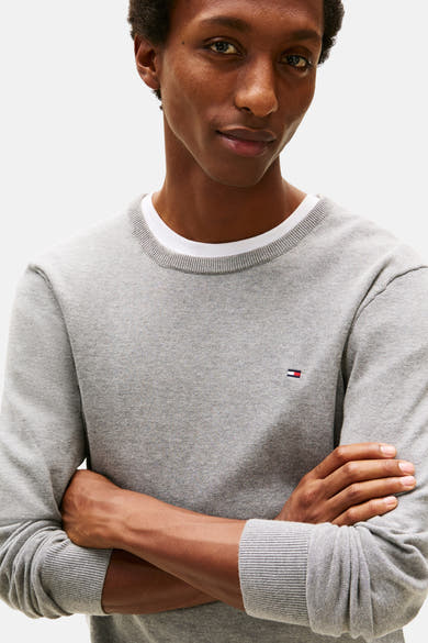 Grijze rondehals trui van Tommy Hilfiger, gedragen met een wit T-shirt met ronde hals, lange mouwen en logo op de borst.