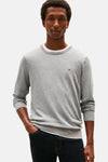 Grijze rondehals trui van Tommy Hilfiger, gedragen over een wit T-shirt, met een donkerblauwe jeans.