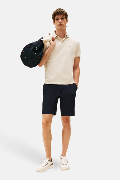Polo beige à manches courtes de TOMMY HILFIGER, porté avec un short bleu marine et des chaussures blanches.