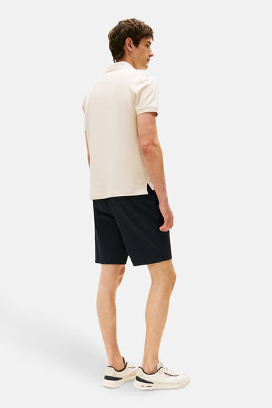 Polo beige à manches courtes de TOMMY HILFIGER, porté avec un short bleu marine et des baskets blanches.