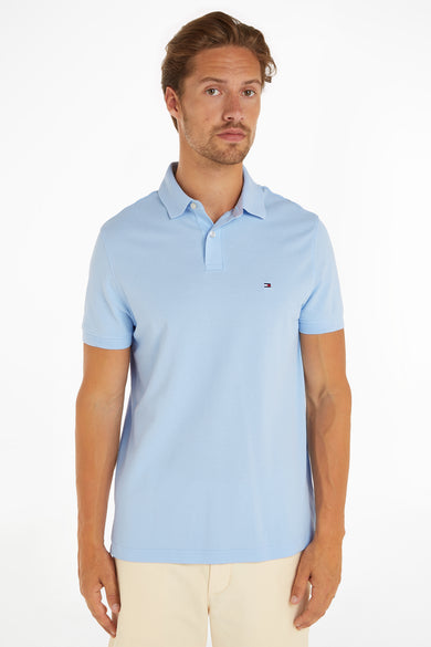 Light blue piqué polo shirt by Tommy Hilfiger, featuring small logo on chest, worn with cream pants, front view.