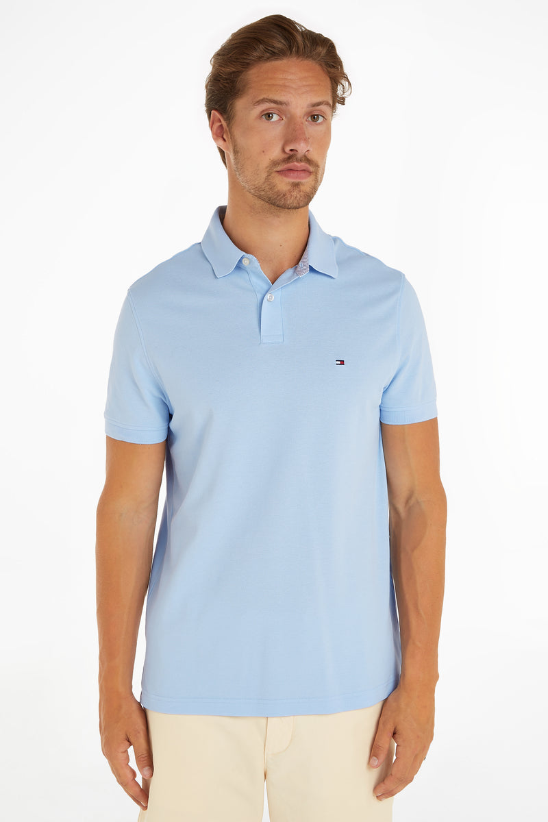 Light blue piqué polo shirt by Tommy Hilfiger, featuring small logo on chest, worn with cream pants, front view.