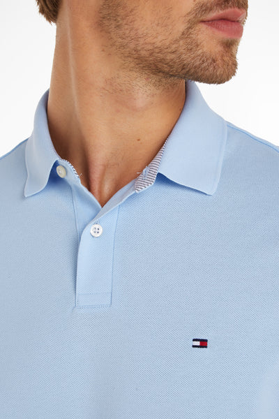 Light blue piqué polo shirt by Tommy Hilfiger, featuring white buttons and small flag logo on chest, close-up front view.