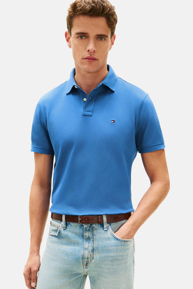 Polo à manches courtes bleu de TOMMY HILFIGER, porté avec un jean clair et une ceinture en cuir marron.