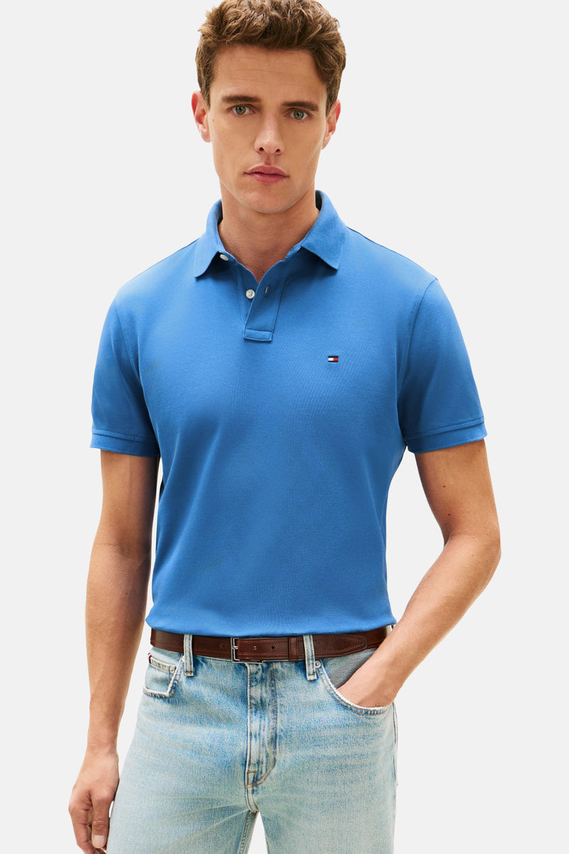 Polo à manches courtes bleu de TOMMY HILFIGER, porté avec un jean clair et une ceinture en cuir marron.