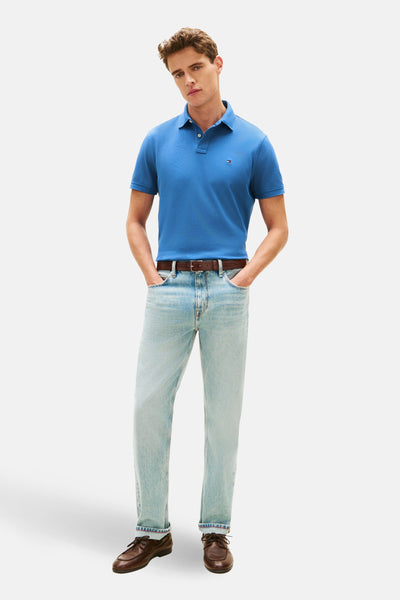 Polo bleu à manches courtes de TOMMY HILFIGER, porté avec un jean délavé, une ceinture marron et des chaussures bateau.