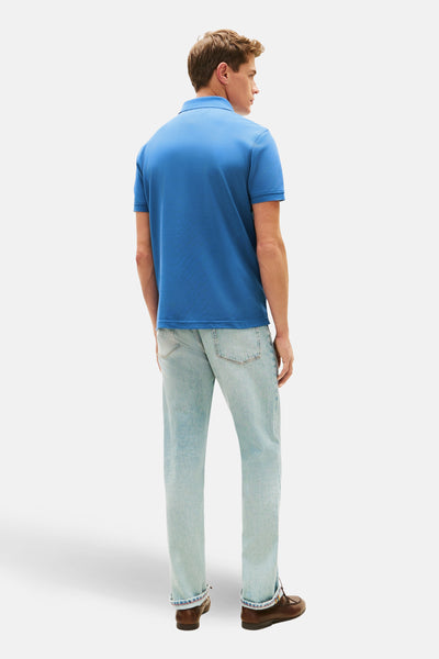 Polo bleu à manches courtes de TOMMY HILFIGER, porté avec un jean délavé et des chaussures bateau marron.