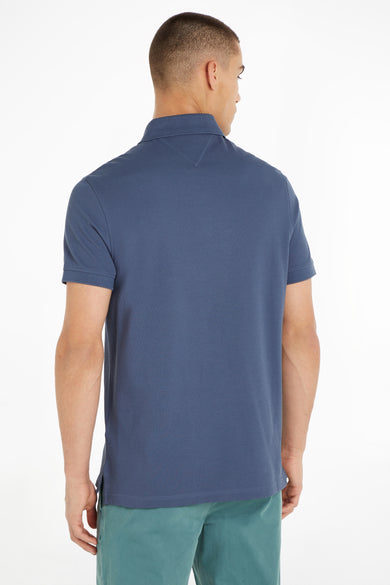 Blue short-sleeve polo shirt with ribbed collar and textured piqué fabric, back view on model wearing teal pants