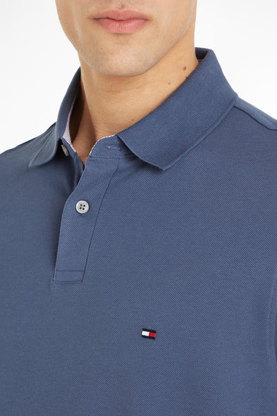 Blue short-sleeve polo shirt by Tommy Hilfiger, featuring ribbed texture, classic collar, and small flag logo on chest, close-up front view