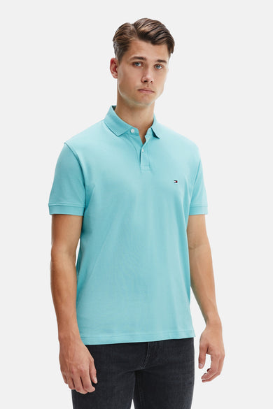 Polo bleu à manches courtes de TOMMY HILFIGER, porté avec un pantalon foncé en denim.