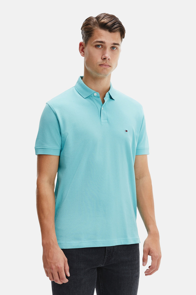 Polo bleu à manches courtes de TOMMY HILFIGER, porté avec un pantalon foncé en denim.