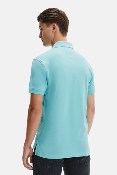 Polo à manches courtes bleu de Tommy Hilfiger, vu de dos, porté avec un pantalon noir.
