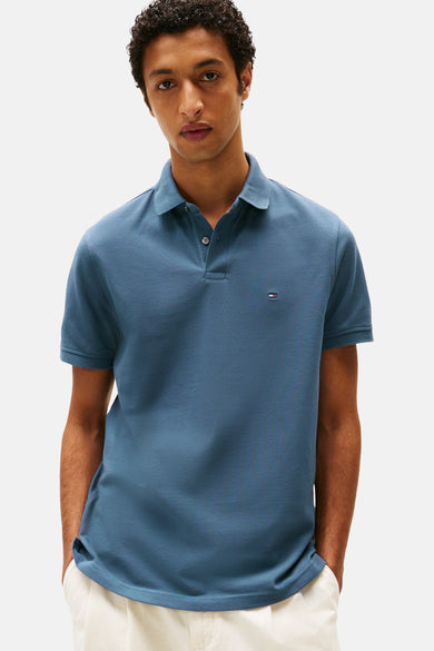 Polo bleu à manches courtes par TOMMY HILFIGER, porté par un homme aux cheveux bouclés.