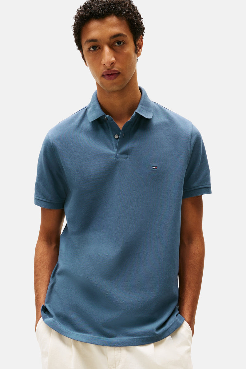 Polo bleu à manches courtes par TOMMY HILFIGER, porté par un homme aux cheveux bouclés.
