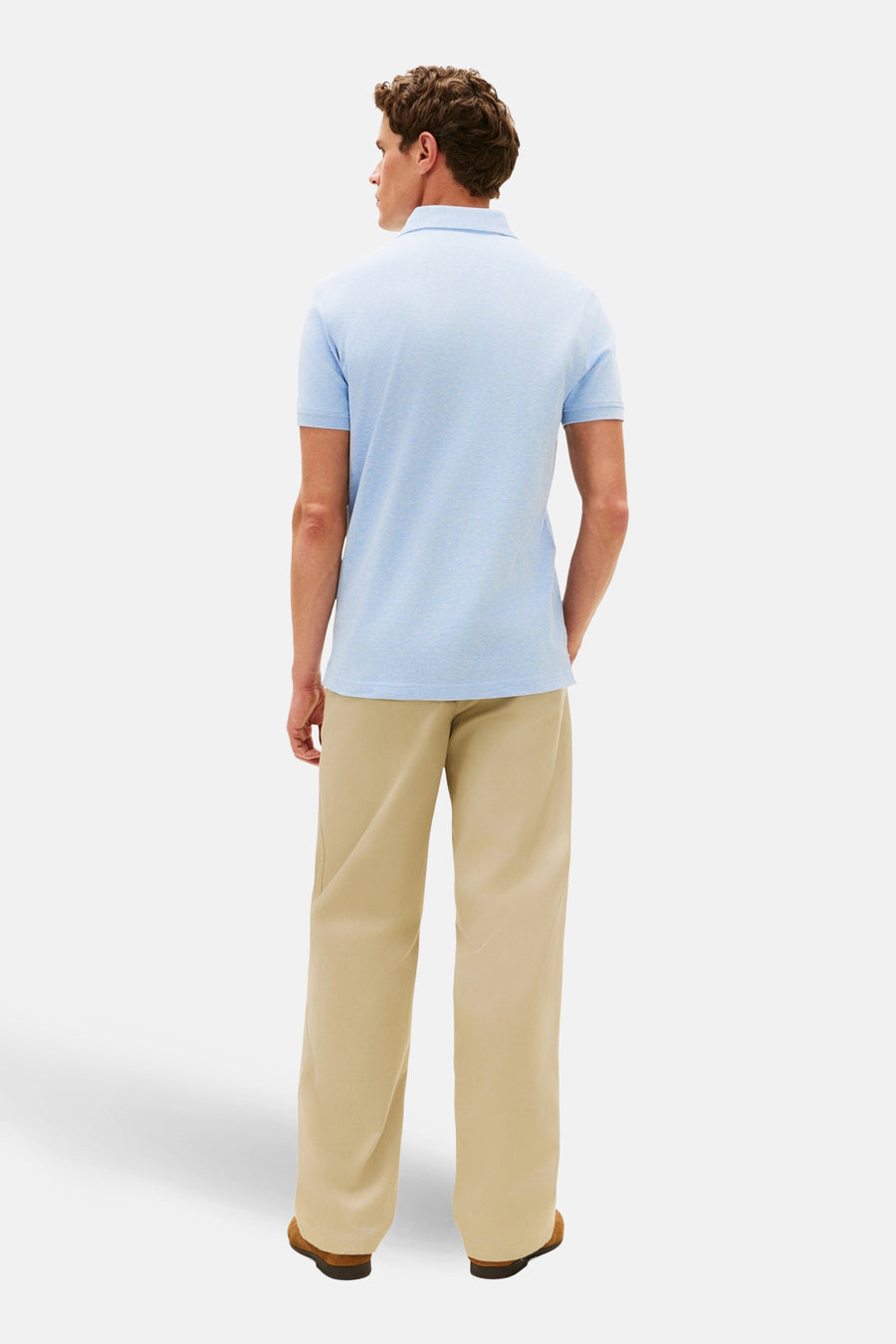 Polo à manches courtes bleu de Tommy Hilfiger, vu de dos, porté avec un pantalon beige et des chaussures marron.