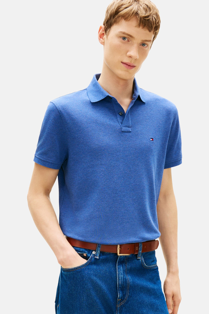 Polo bleu à manches courtes de TOMMY HILFIGER, porté avec un jean bleu et une ceinture en cuir marron.

